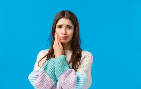 Health, stomatology concept. Silly cute woman in winter sweater, complaining on toothache, having decay or rotten tooth, touching cheek frowning and sulking from pain, waiting in dentist office